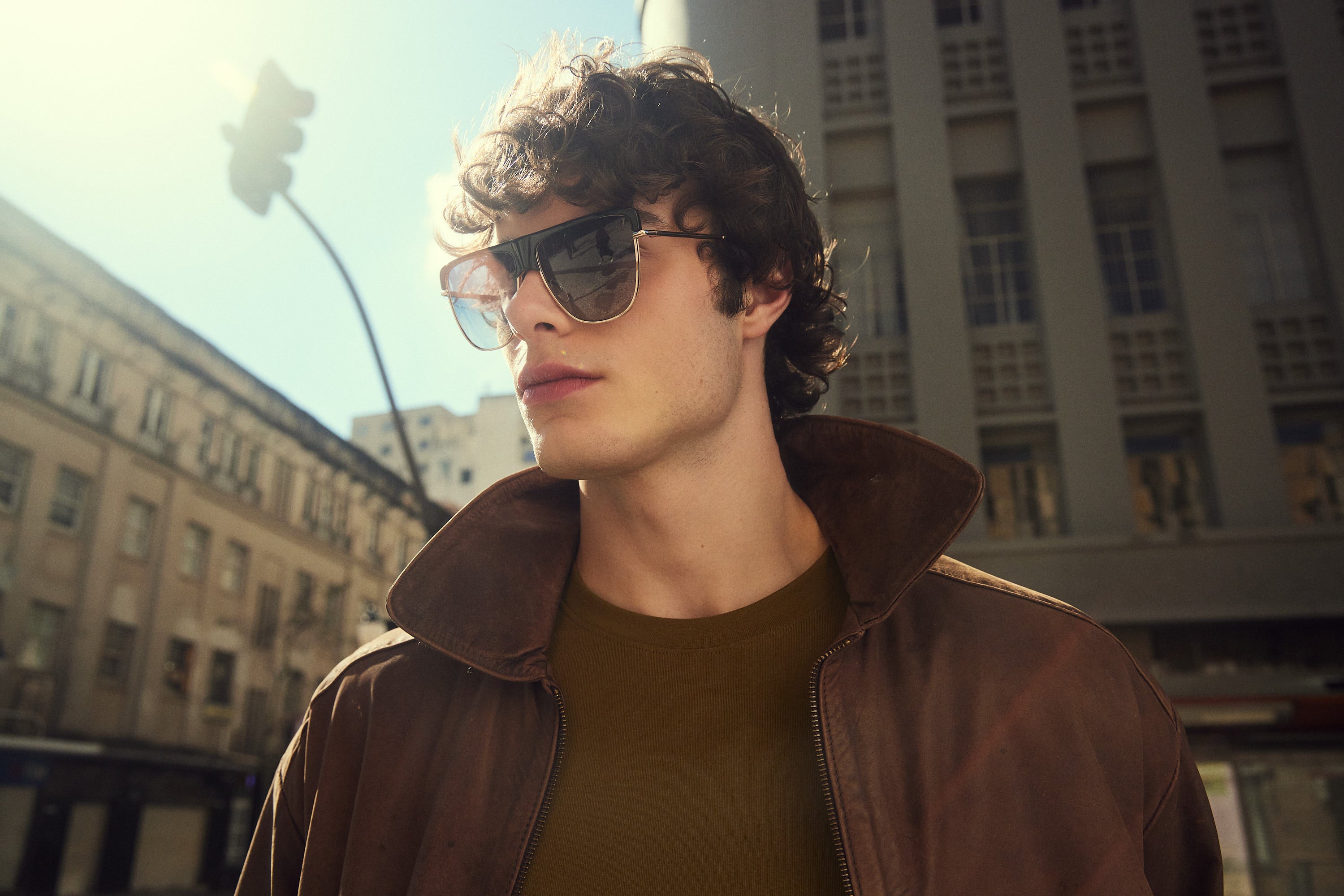 An image banner to shop sunglasses with a man wearing dark shield sunglasses with a brown leather jacket.