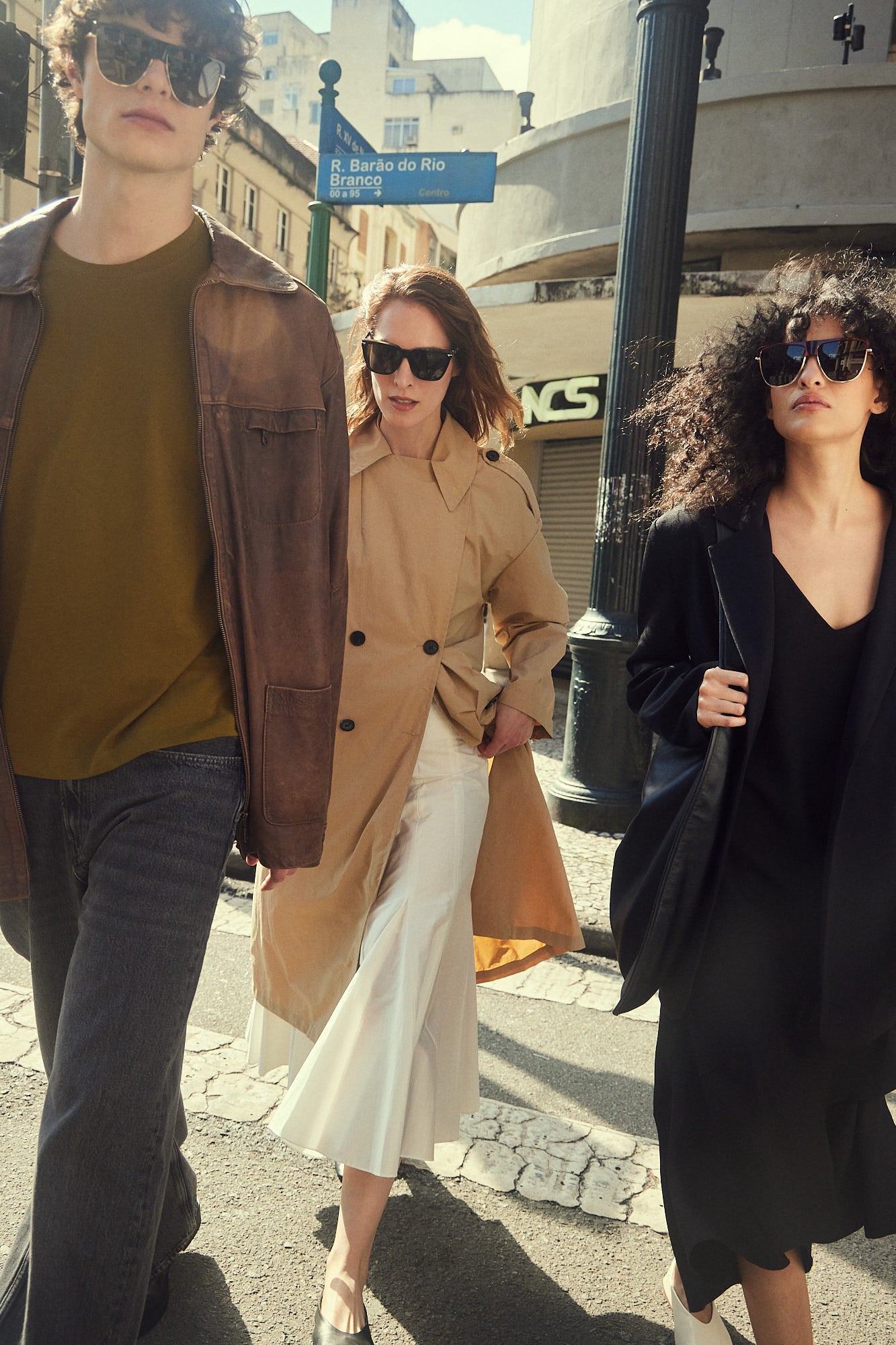 Three models walking outdoors on a city street wearing  polarized quality sunglasses, fashion jackets, and dresses. 