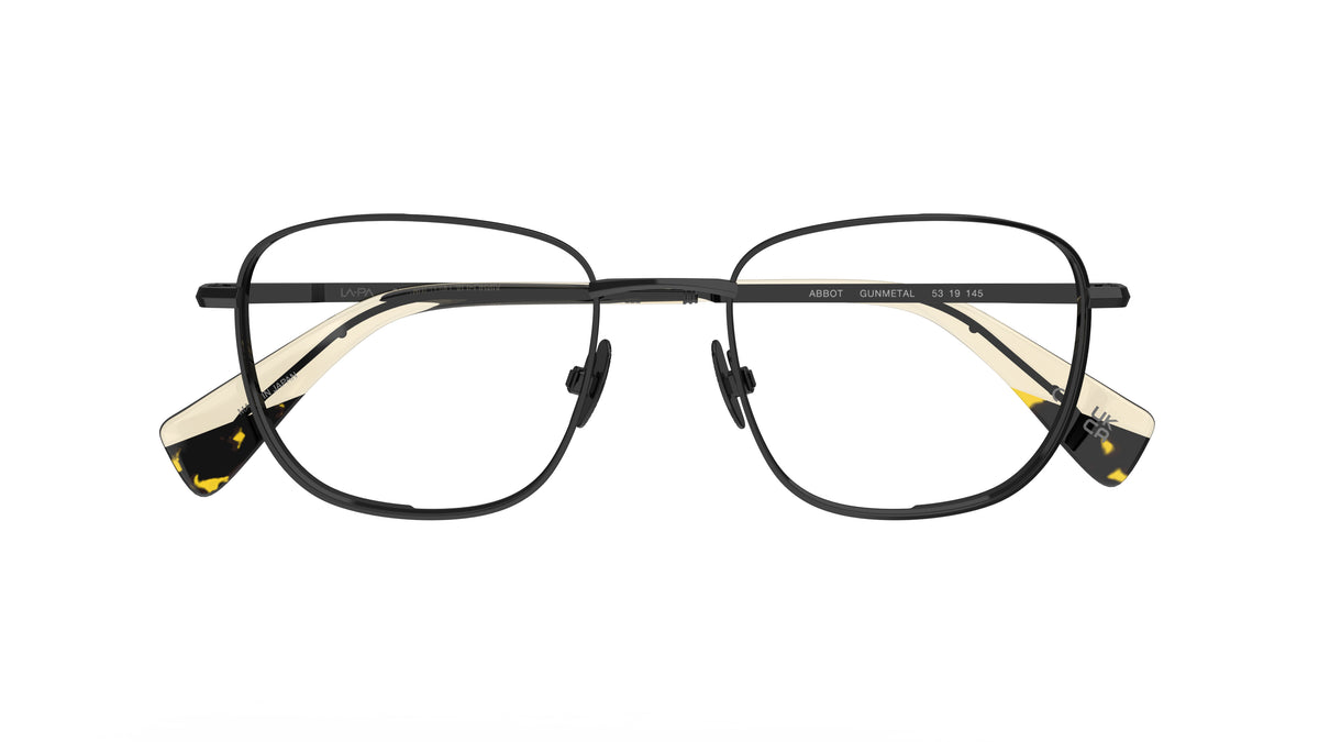 A pair of square gunmetal navigator titanium eyeglass frames with nosepads and cream acetate accents at the temple tips, shown against a plain white background.