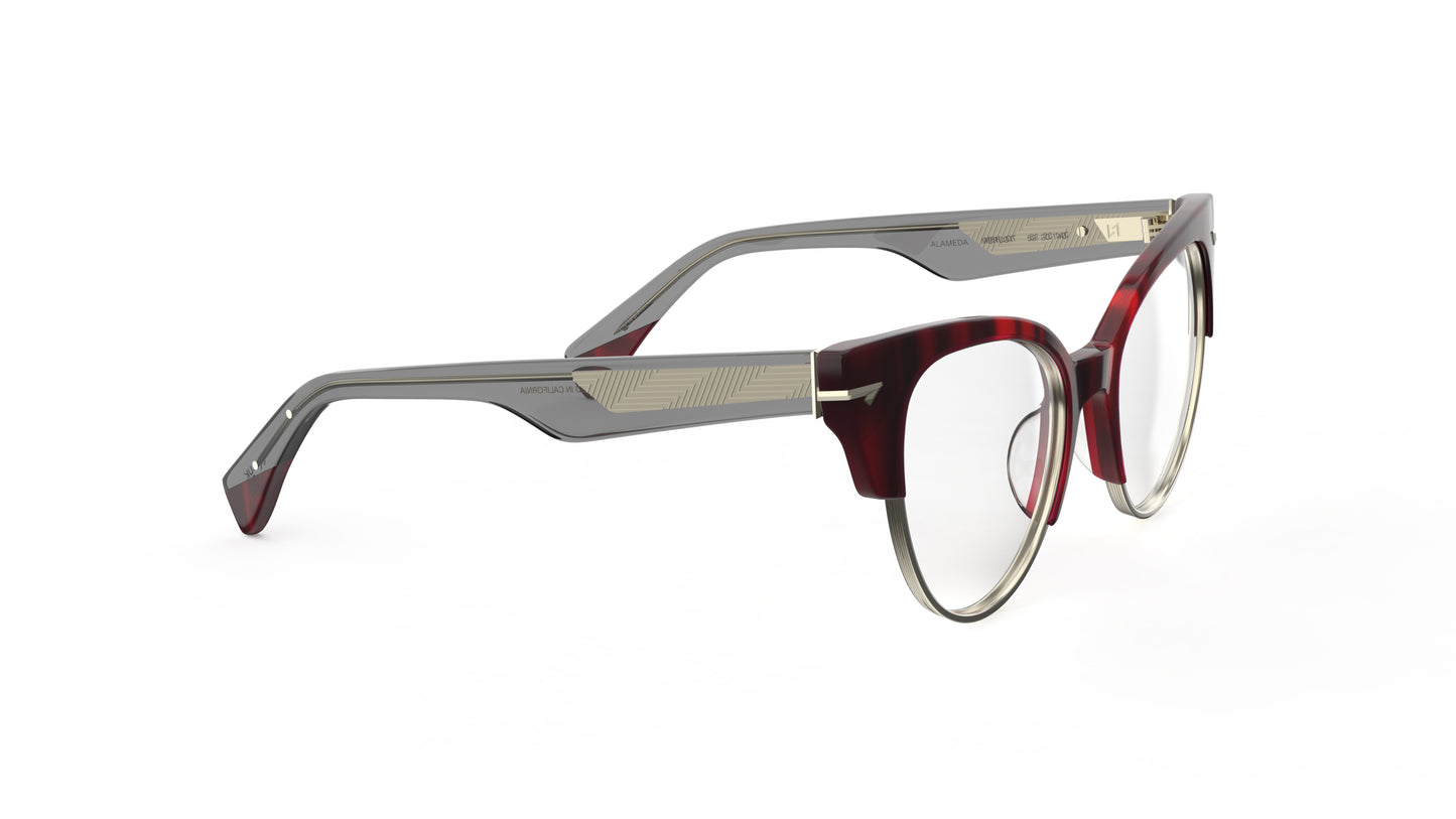 A pair of cat-eye eyeglasses featuring a dark red merlot colored front with sculpted rivets, translucent gray acetate temples featuring a geometric patterned metal wire core.