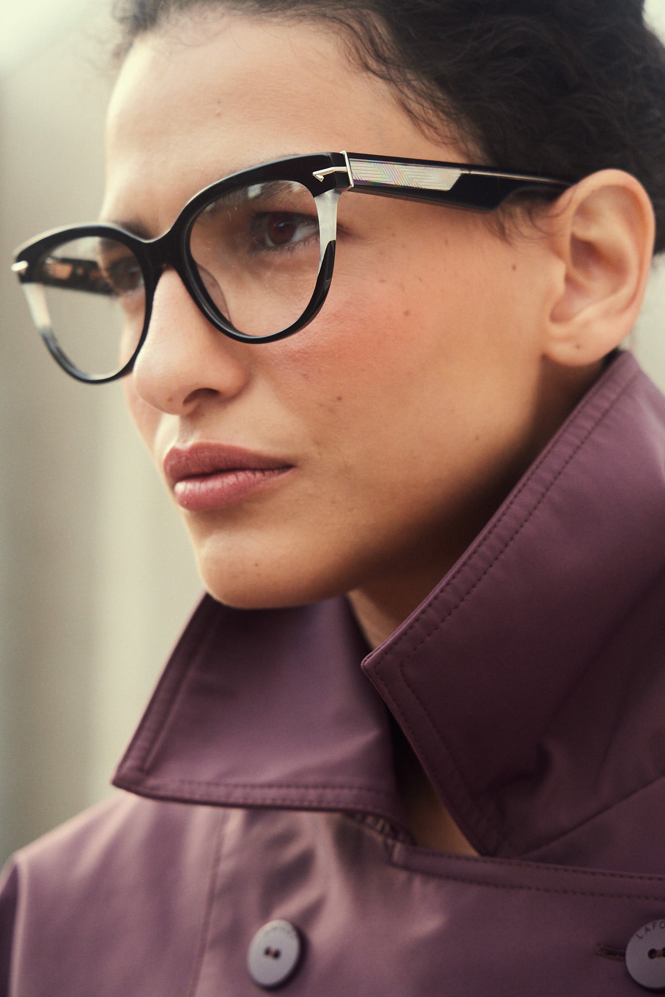 A close-up portrait of a woman wearing black and pearl white cat-eye acetate eyeglasses and a dark purple high-collar jacket.