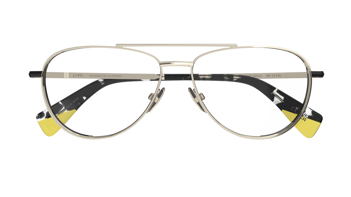 A pair of aviator-style eyeglasses with a light gold titanium construction, black havana and yellow acetate tips on a white background.