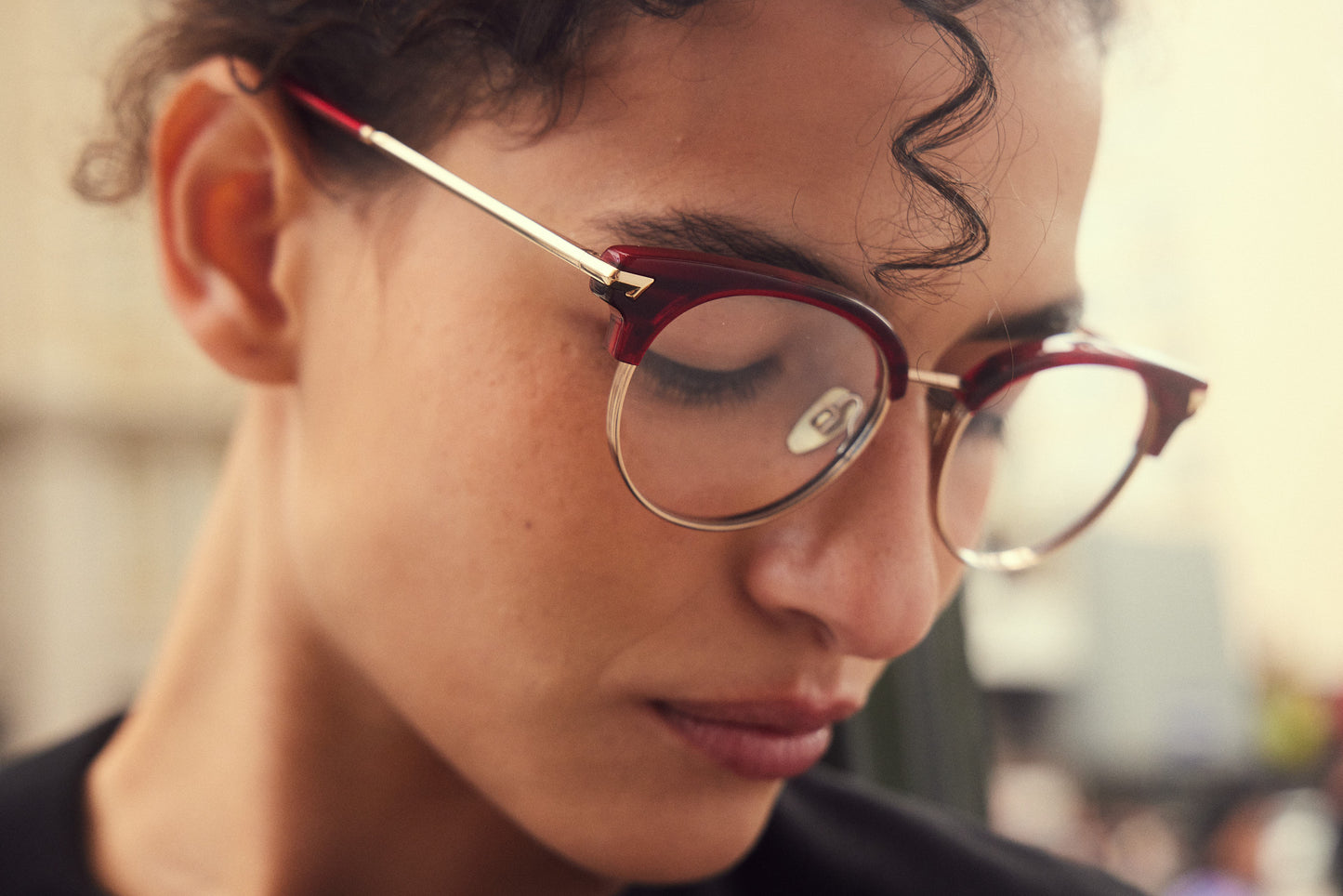 A close-up shot of a woman wearing round clubmaster eyeglasses with a dark red merlot acetate frame and gold titanium rims,nosepads and hinges.